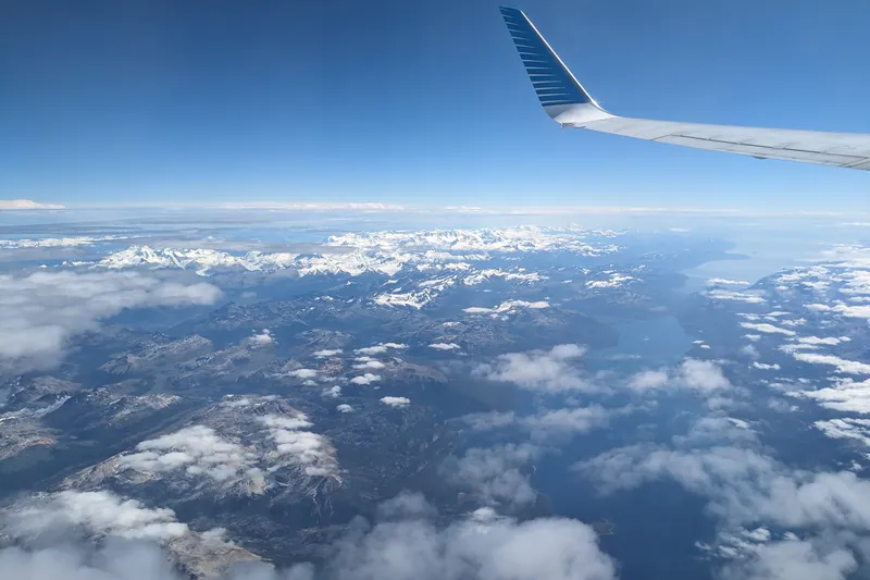 Blick aus dem Flugzeug auf Tragfläche, Wolken und verschneite Berge