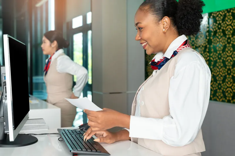 Lächelnde Mitarbeiterin am Schalter prüft ein Ticket und tippt am Computer