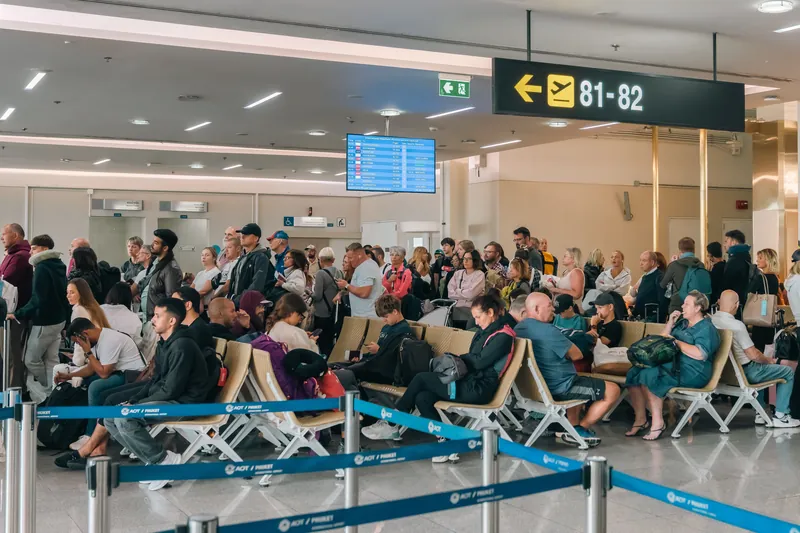 Volle Wartehalle am Gate, viele Reisende sitzen und stehen zwischen Absperrbändern